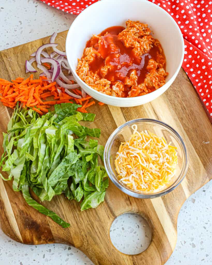 Buffalo Chicken Wraps are made with buffalo sauce, ready-cooked rotisserie chicken breasts, shredded romaine lettuce, thin slices of red onion, shredded carrots, and shredded cheddar and Monterey Jack Cheese, all drizzled with your favorite bottled ranch or bleu cheese dressing. 