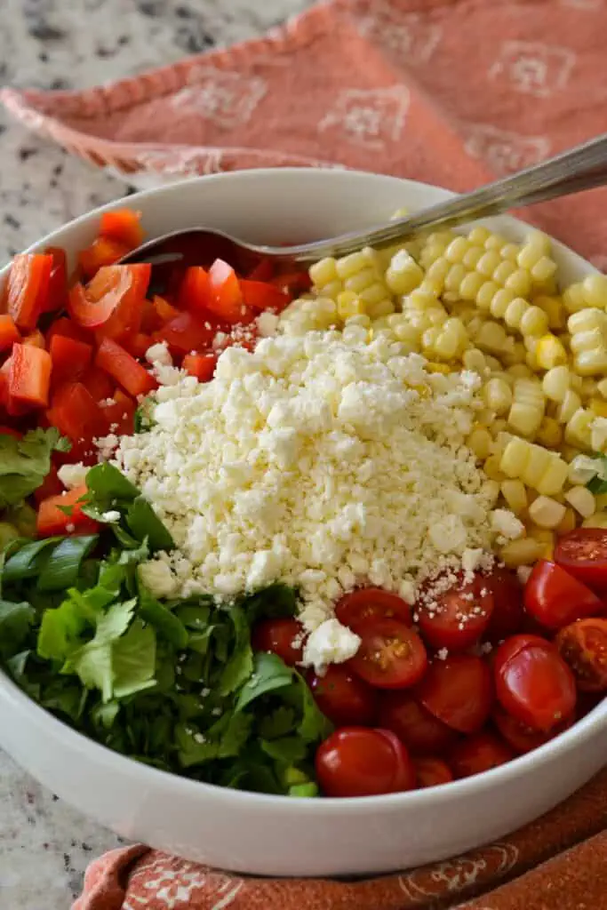 Grab a large bowl and add the cooked corn, diced red peppers, grape tomato halves, cilantro, green onions, minced jalapenos, feta, and red onion. Drizzle with the lime vinaigrette and toss to coat.