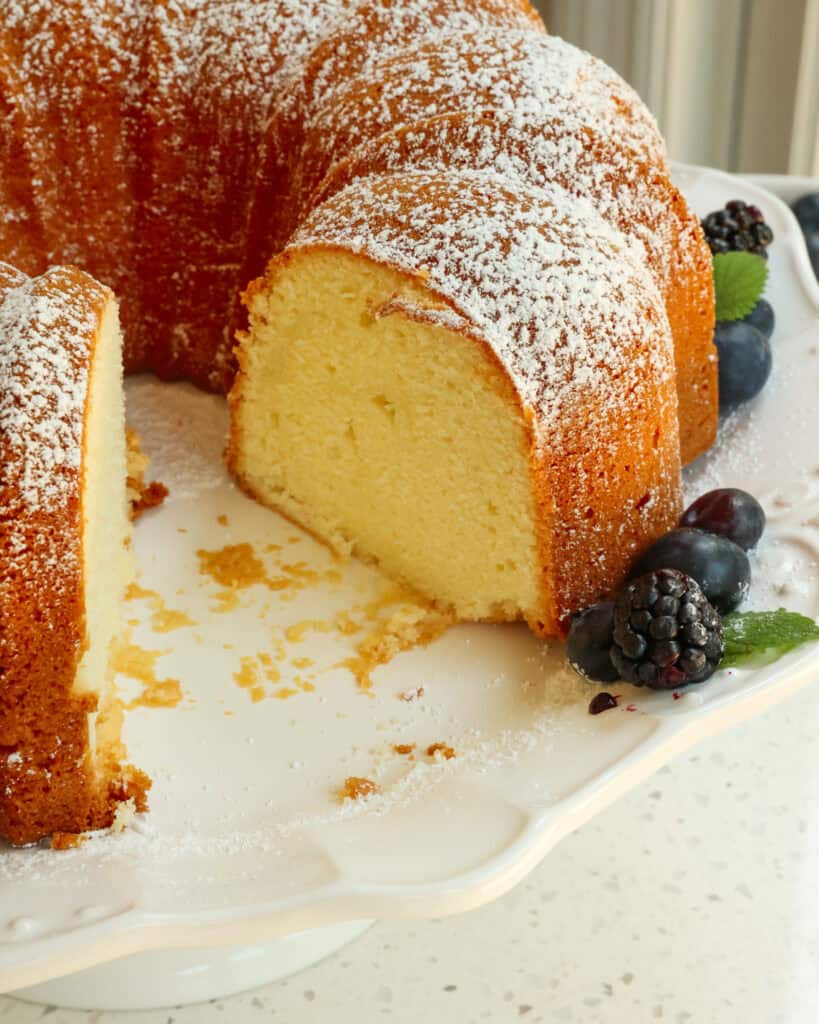 Cream cheese pound cake on a cake plate with a slice removed. 