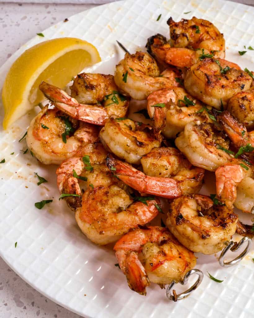 A close up of grilled shrimp on a white plate with a lemon wedge.