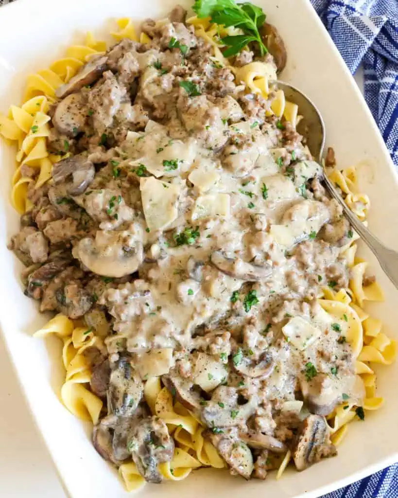 Beef stroganoff with mushrooms and onions over egg noodles in a bowl with a spoon. 