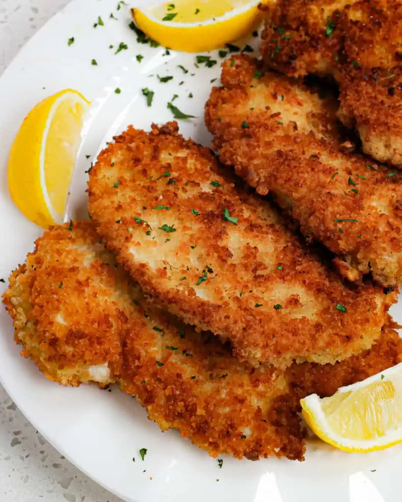 Chicken schnitzel on a plate with fresh lemon wedges. 