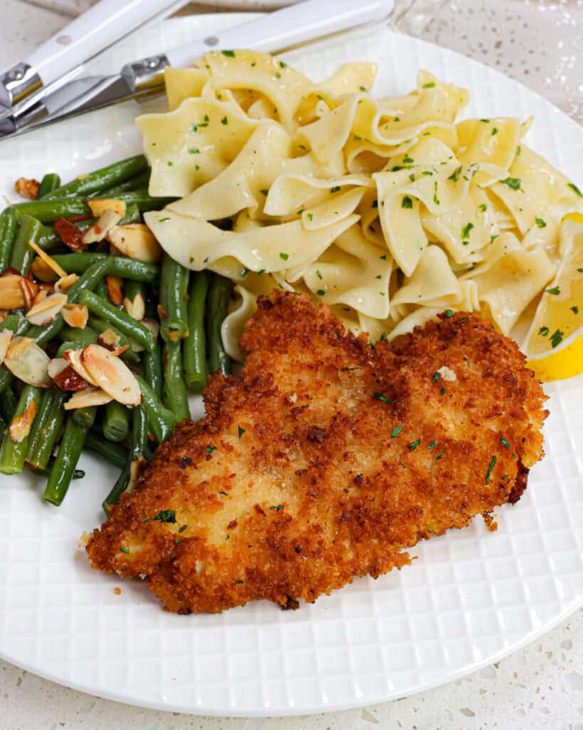 A serving plate full of chicken schnitzel, buttered egg noodles, and green beans almondine. 
