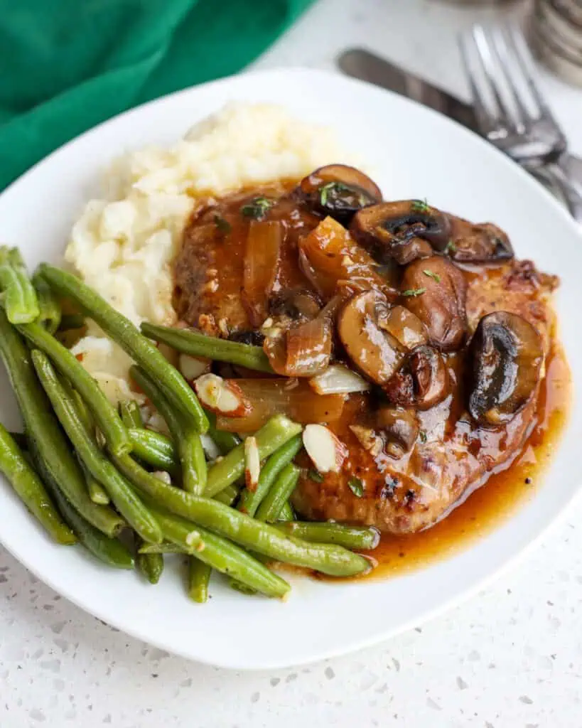 Cube steak smothered in gravy over mashed potatoes with a side of green beans.