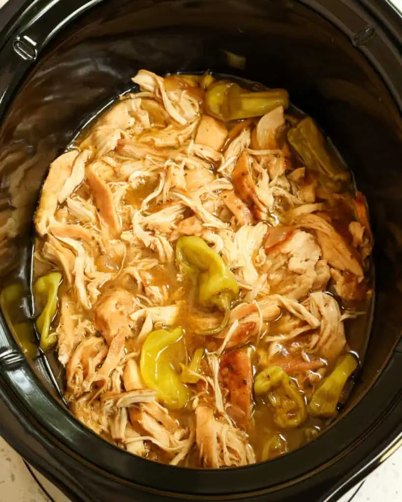 A black crock pot full of mississippi chicken. 