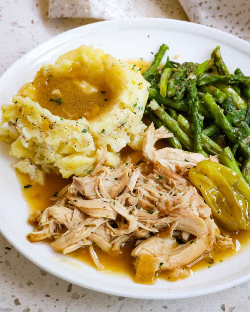 Mississippi chicken, mashed potatoes, and sauteed asparagus on a single serving white plate. 