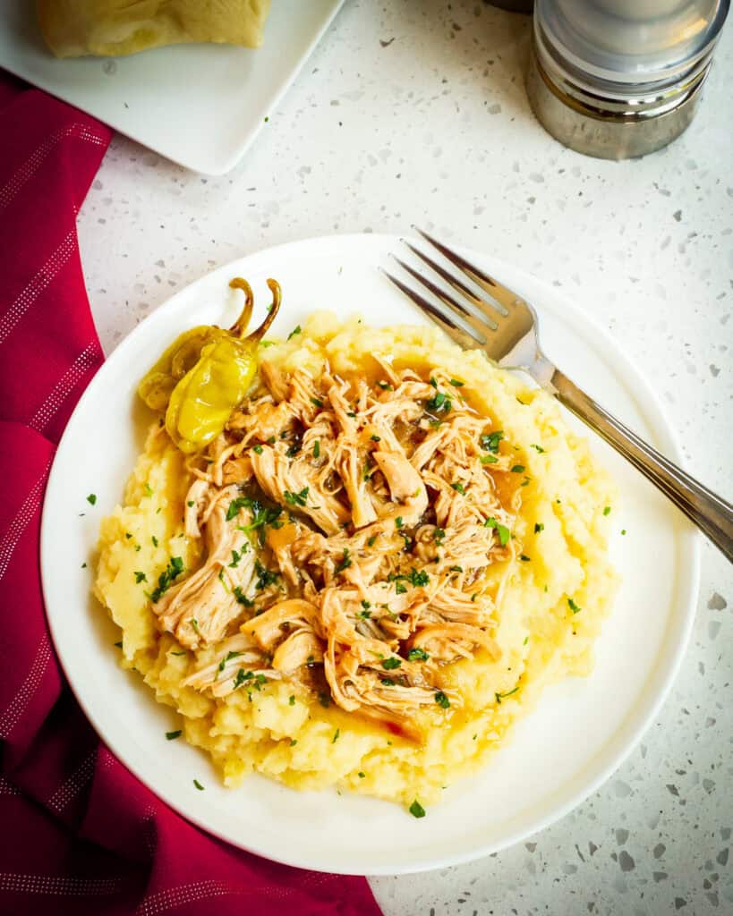 An over head view of mississippi chicken over mashed potatoes on a single serving plate  