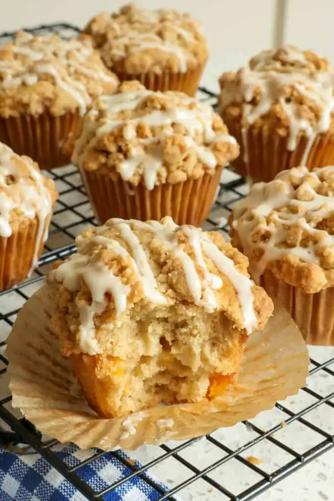 These bakery-style Peach Muffins have a melt-in-your-mouth crumb topping and a maple vanilla drizzle.