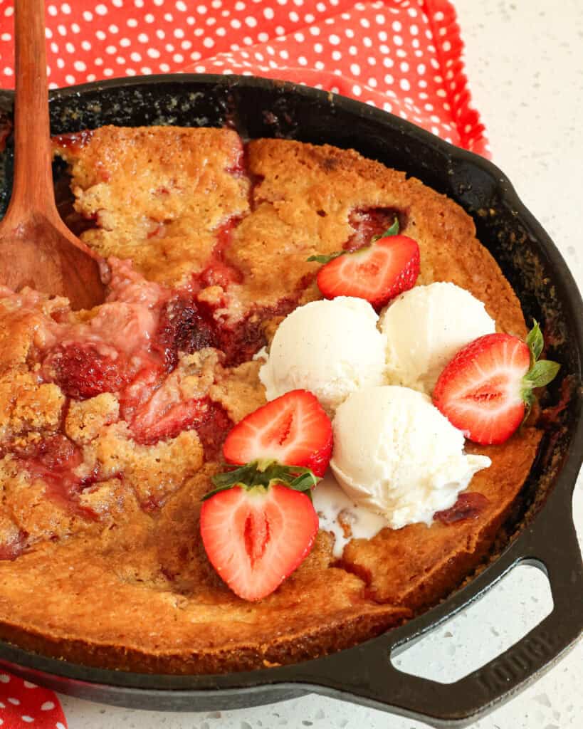 Strawberry Cobbler in a cast iron skillet with ice cream and strawberries on top.