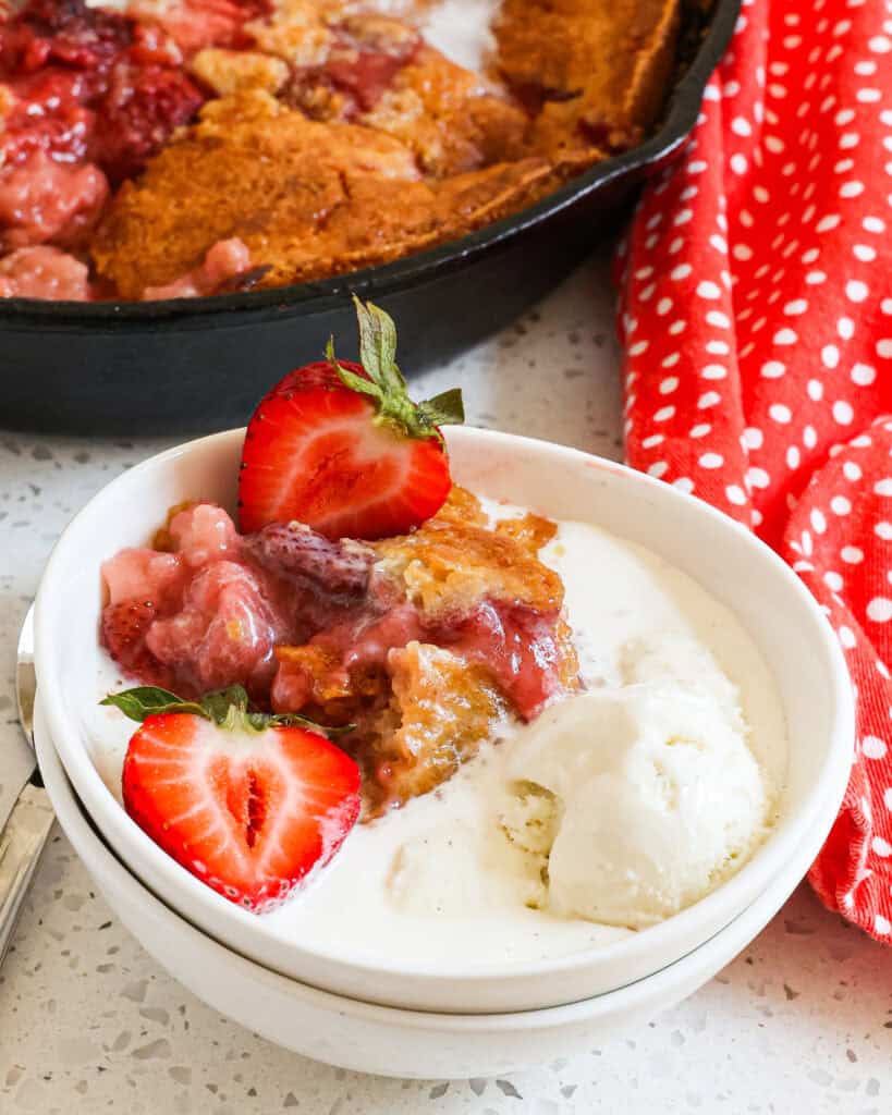 Close up of Strawberry Cobbler in a small white bowl with ice cream and fresh halved strawberries.
