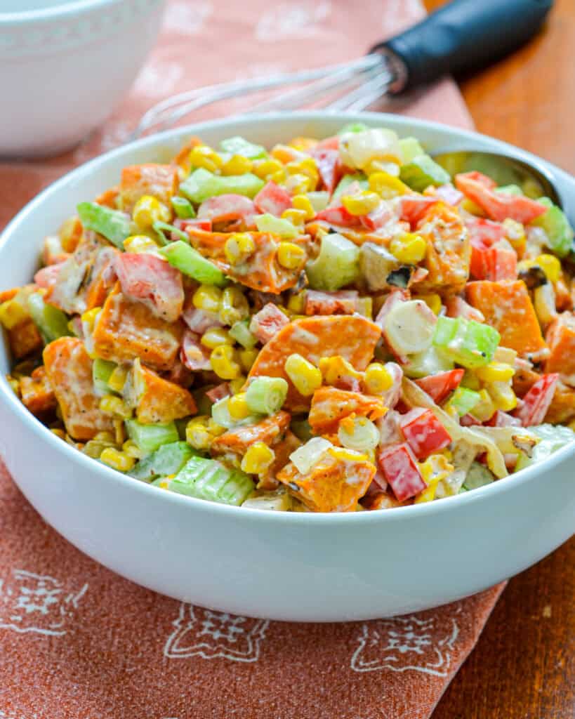 A large white serivng bowl filled with sweet potato salad with a whisk in the background. 