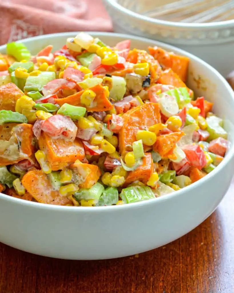 A close up view of sweet potato salad with blackened corn, sweet onion, crisp celery, red bell pepper, and scallions all in creamy salsa dressing.