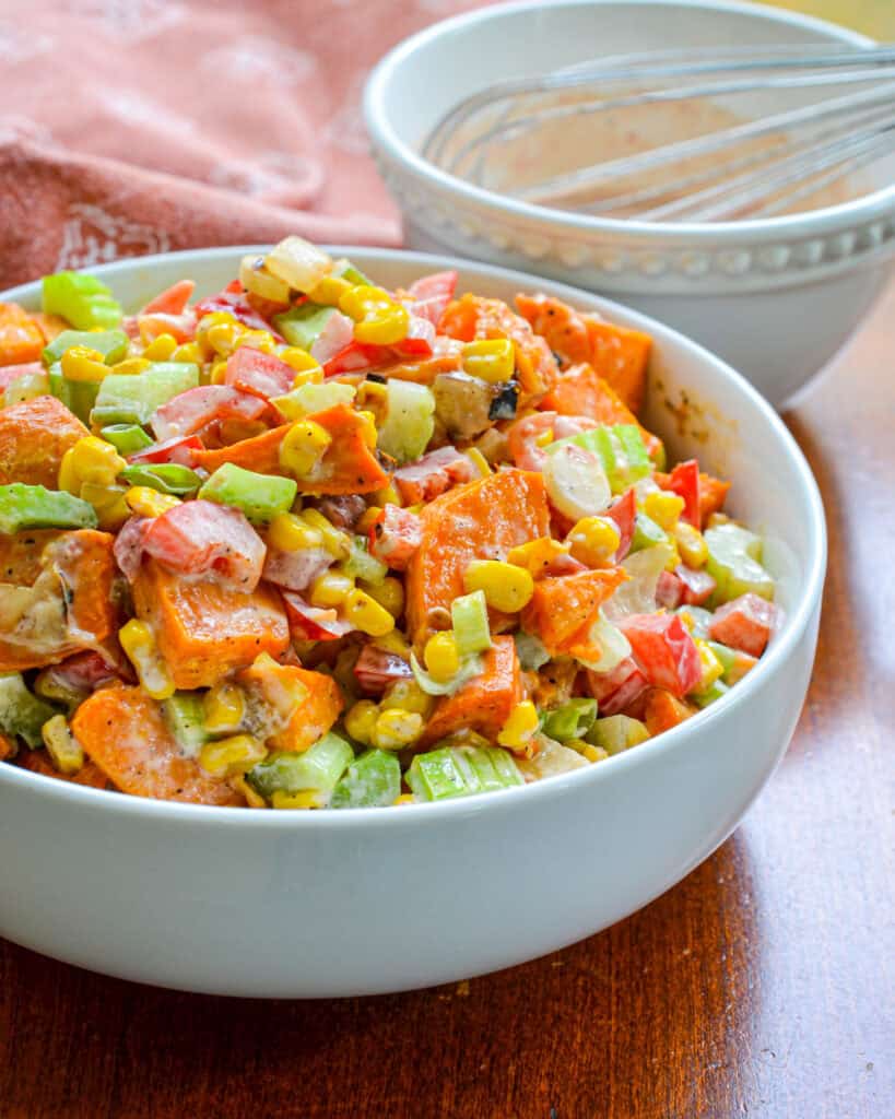 A large white bowl full of sweet potato salad with a small bowl of salsa dressing in the background. 