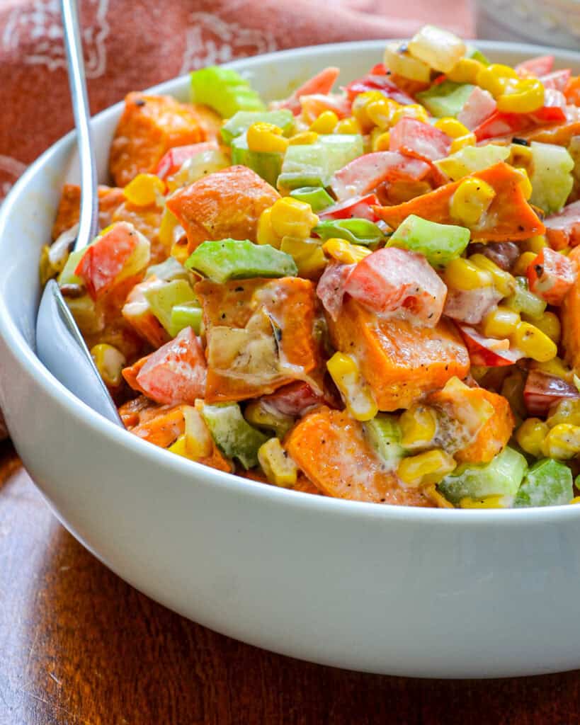 A close up view of sweet potato salad in a large white bowl with a metal spoon. 