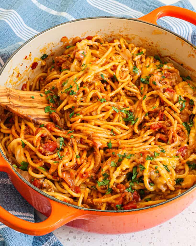 A Dutch oven full of cheesy taco spaghetti with a wooden spatula in a the Dutch oven.