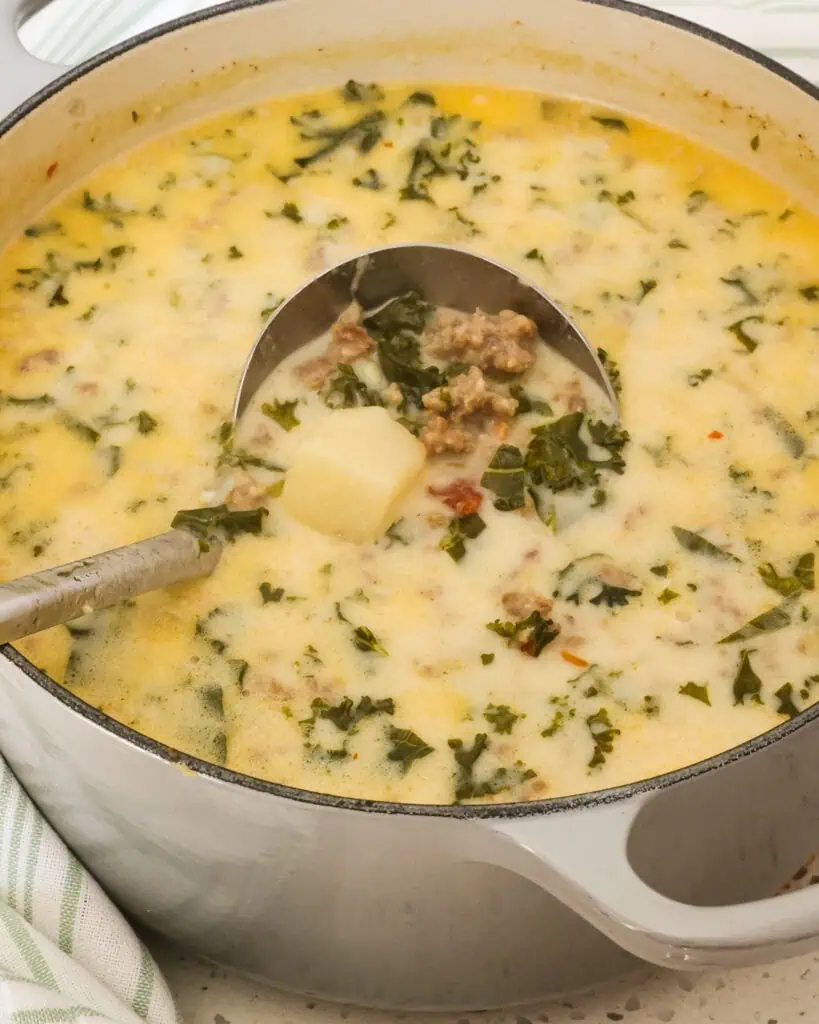 A Dutch oven and a large soup ladle full of zuppa toscana. 