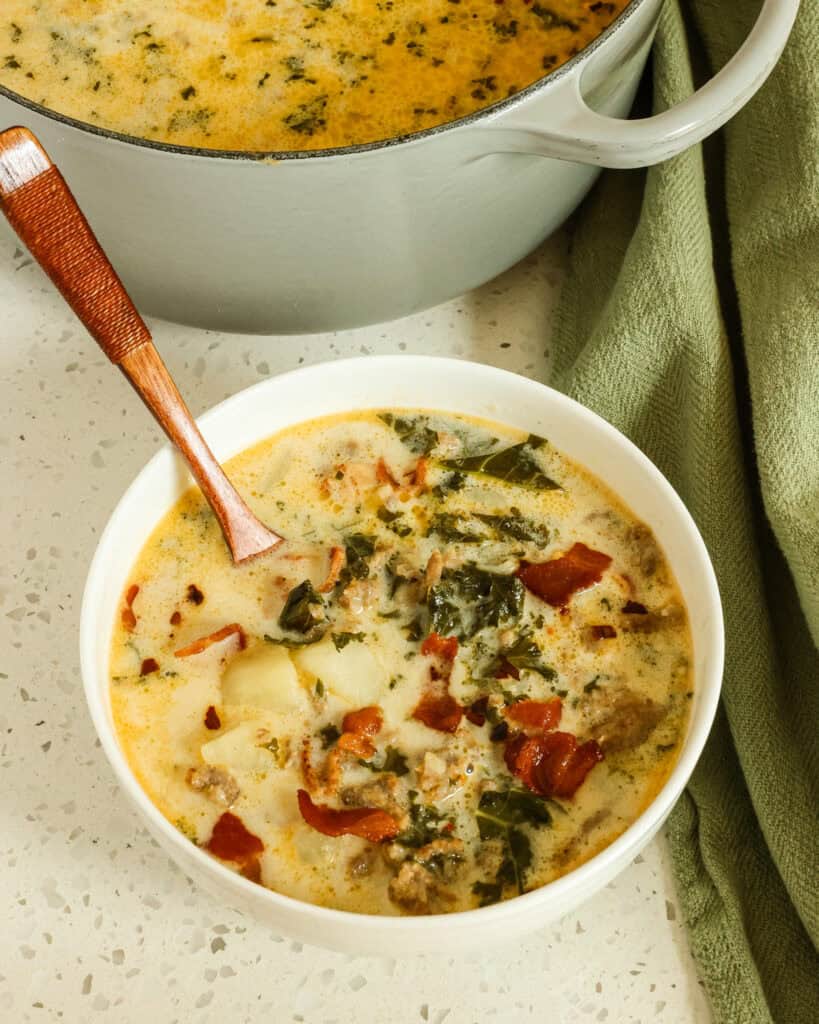 Zuppa Toscana in a bowl with a wooden spoon and a Dutch oven full of zuppa toscana in the background. 