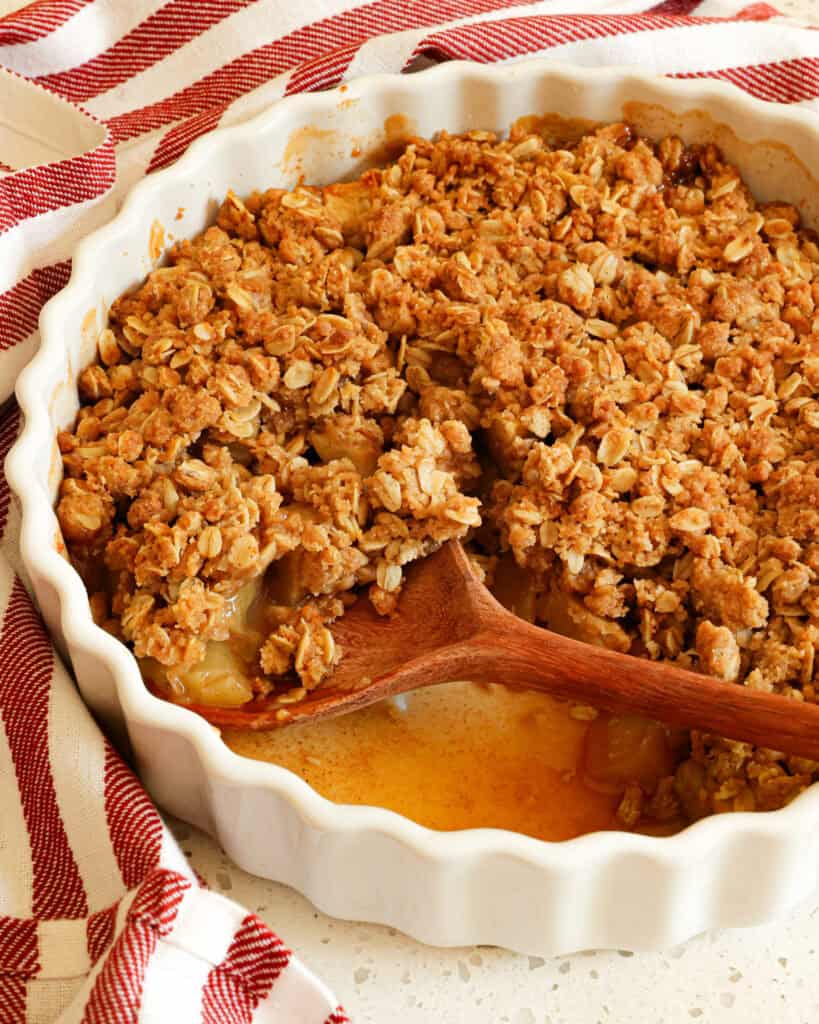 A baking dish full of apple crisp with a wooden spoon in the dish.
