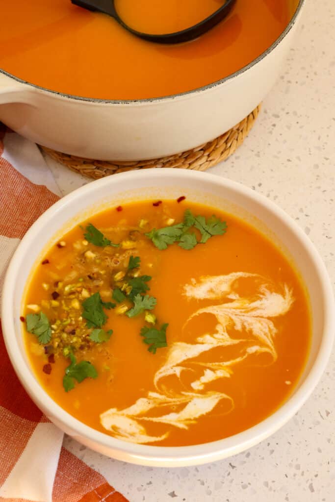 Carrot Soup is both delicious and easy with onions, garlic, and a hint of ginger garnished with chopped pistachios, cilantro, and a swirl of cream.