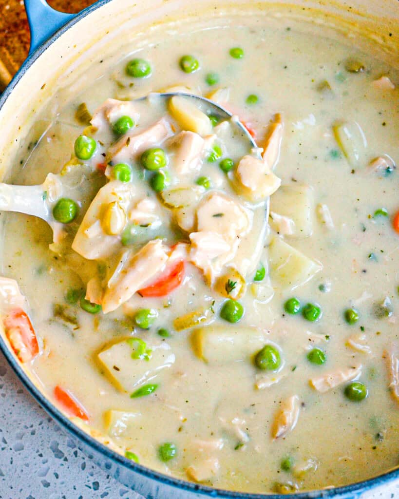 A Dutch oven and a ladle full of chicken pot pie soup. 
