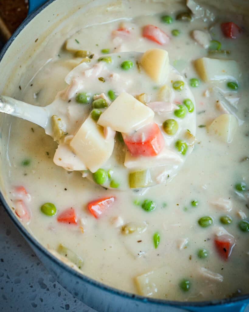 A Dutch oven and a large ladle full of homemade chicken pot pie soup. 