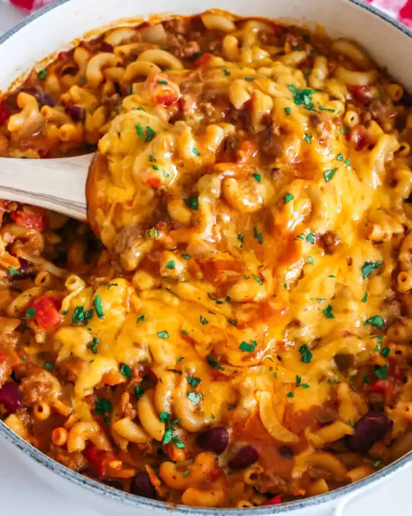 A Dutch oven and a wooden spoon full of cheesy chili mac.