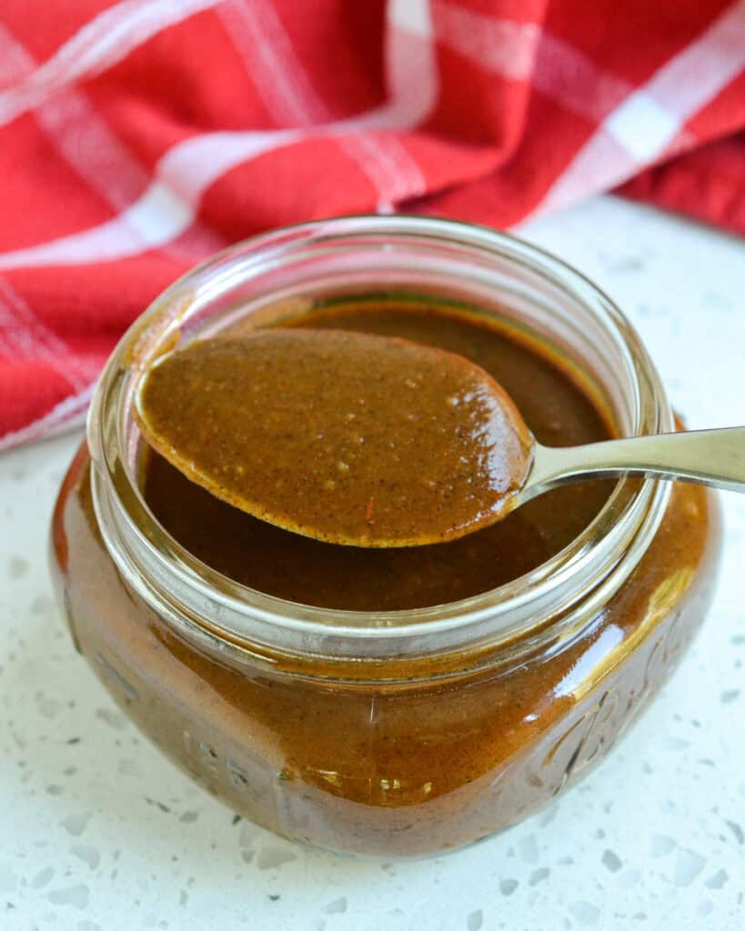 Enchilada Sauce in a small square mason jar with a sauce on the spoon.