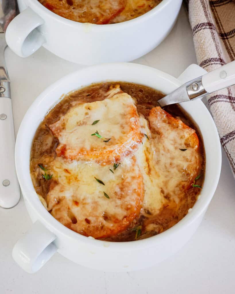 Two crocks full of French Onion Soup with white spoons.