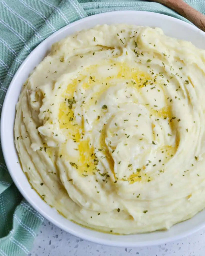 A serving dish full of instant mashed potatoes with butter and chopped parsley. 