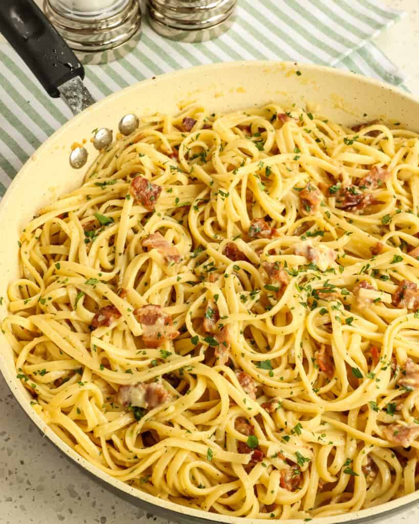Pasta Carbonara in a large skillet with salt and pepper shakers behind.