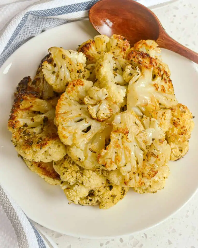 An overhead view of roasted cauliflower on a serving plate with a wooden spoon. 