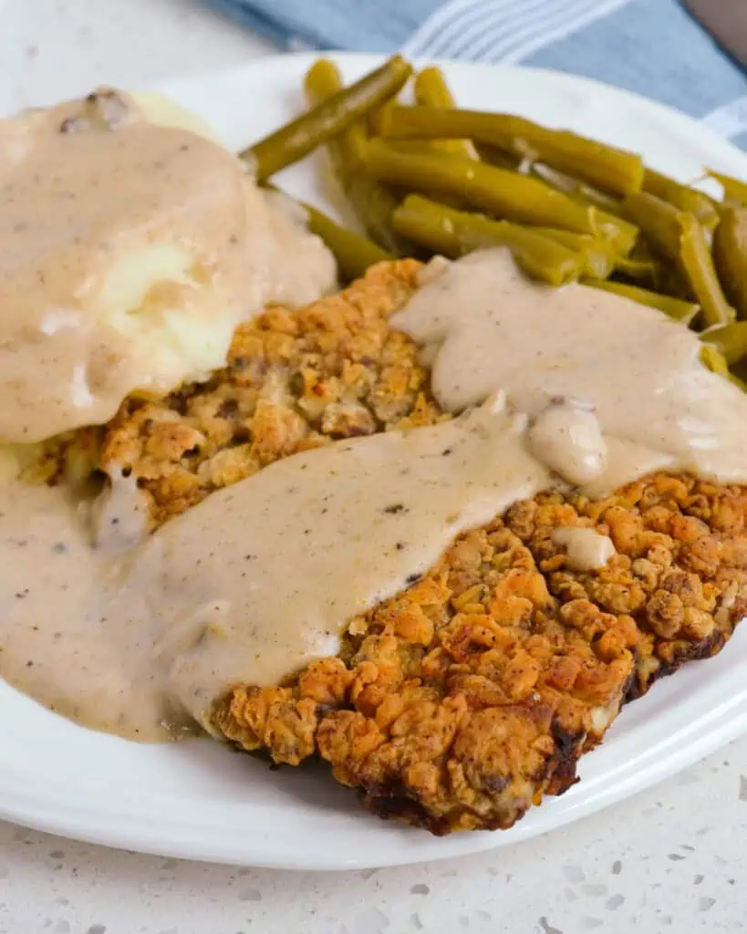 Chicken Fried Steak on a serving plate with country gravy, mashed potatoes, and green beans.
