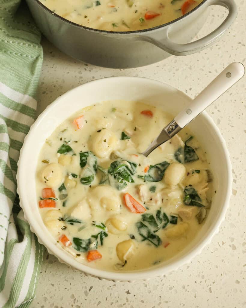 A white bowl full of chicken gnocchi soup with a spoon in it.