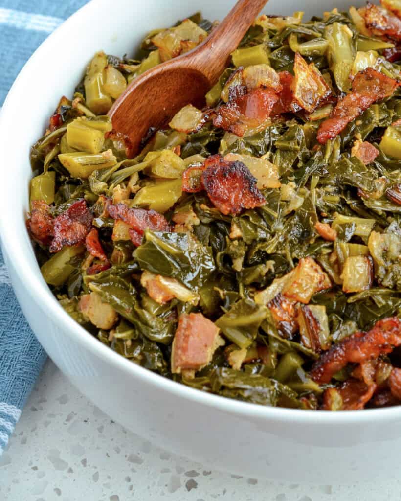 A serving bowl full of collard greens with a wooden spoon in it.