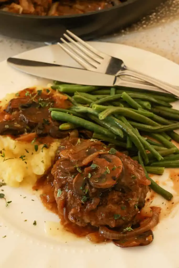 Hamburger Steak and Gravy is classic comfort food at its best, with tender and juicy pan-fried hamburger patties smothered in a tasty brown gravy with plenty of sweet onions.