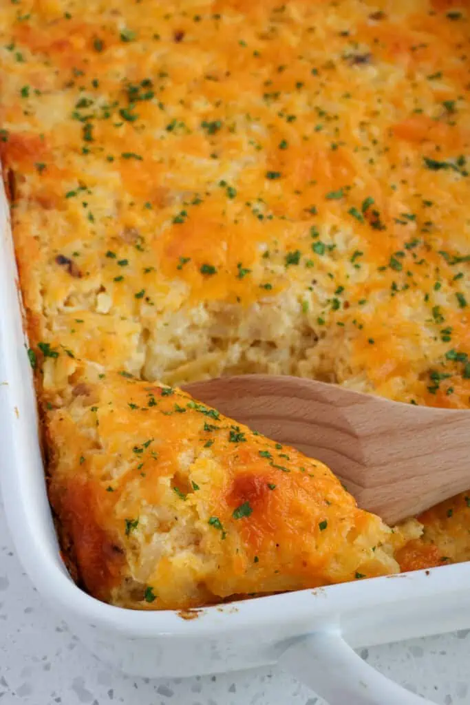 This foolproof hashbrown casserole recipe starts with thawed frozen shredded hash brown potatoes combined with sauteed onions and garlic, sour cream, butter, and a generous portion of cheddar cheese.