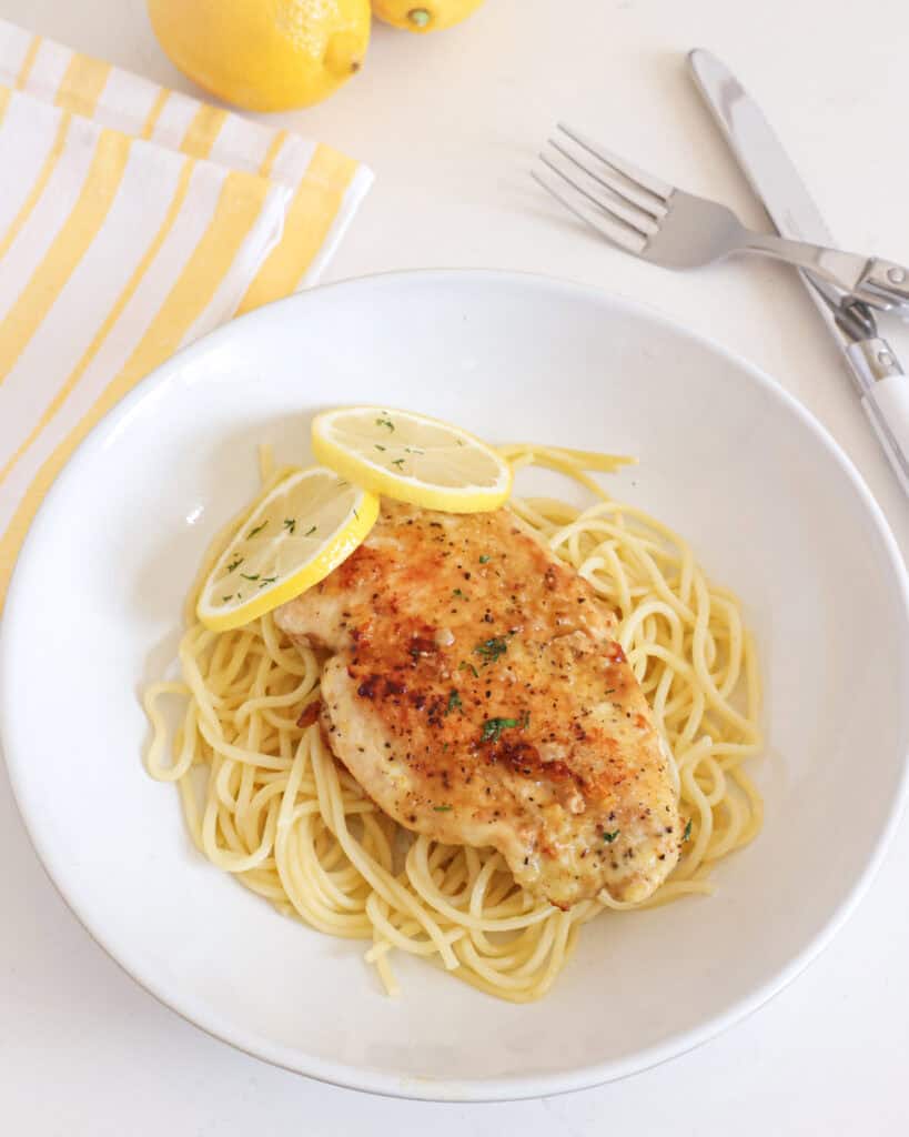 Lemon pepper chicken breast over thin spaghetti in a single serving bolw. 