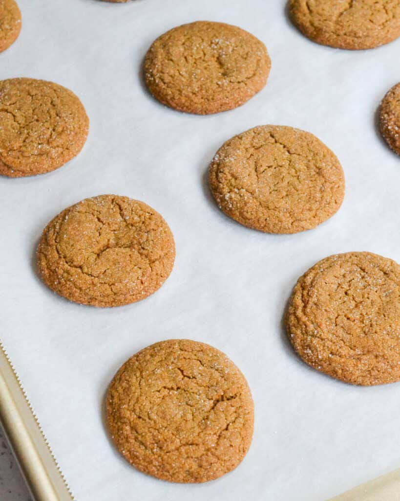 Freshly baked molasses cookies on a baking sheet covered with parchment paper.