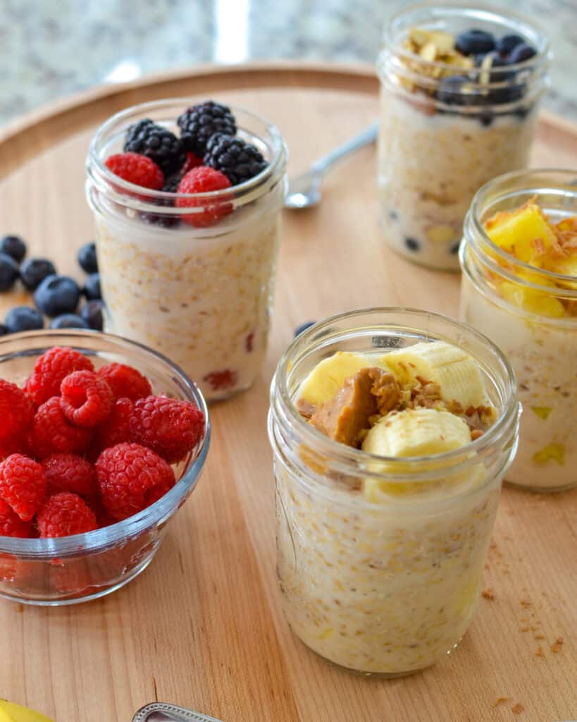 Overnight oat flavor variations in mason jars on a cutting board with fruit around.