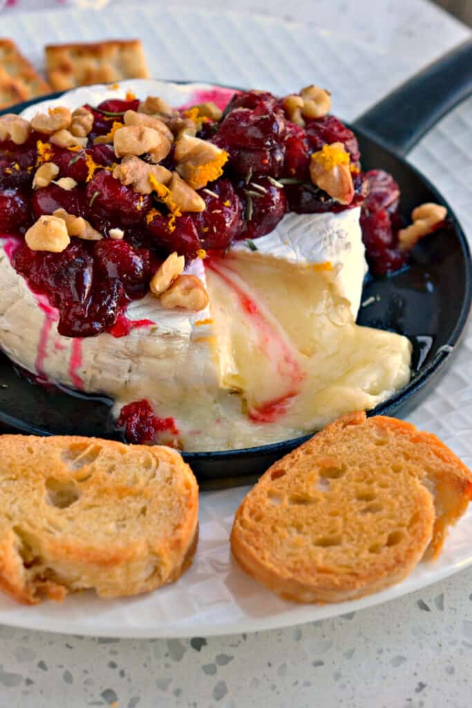 Brie cheese is baked to melted perfection and topped with sweetened cranberries, walnuts, orange zest, and chopped fresh rosemary. 