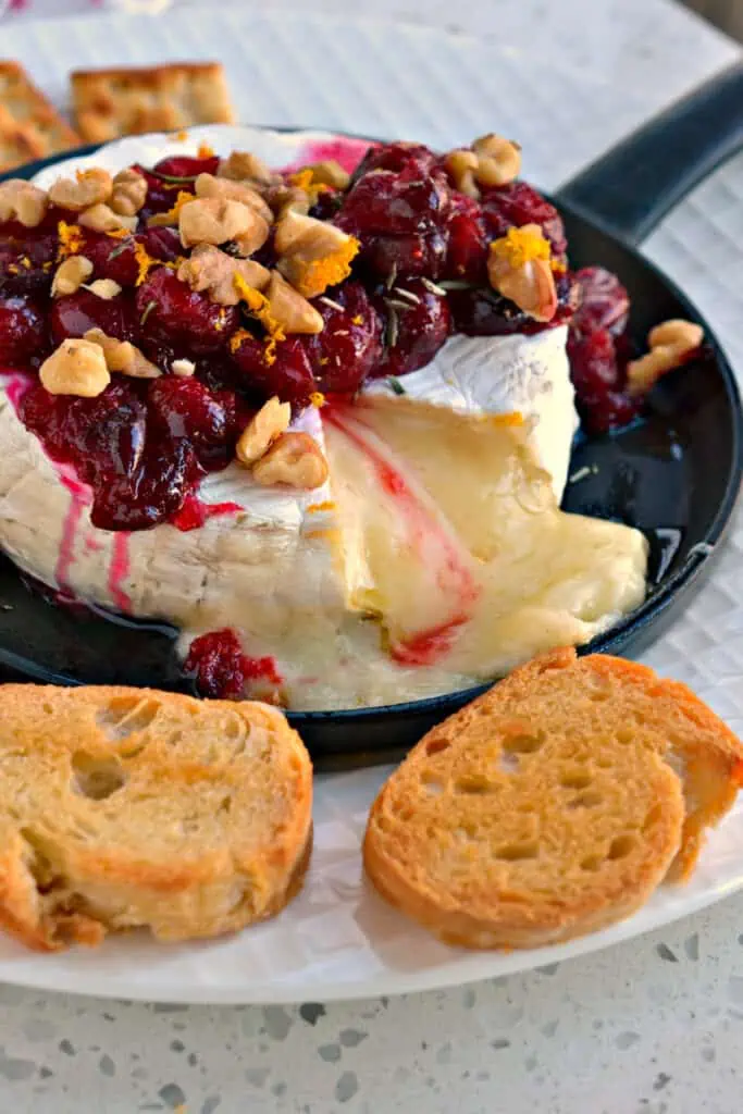 Brie cheese is baked to melted perfection and topped with sweetened cranberries, walnuts, orange zest, and chopped fresh rosemary. 
