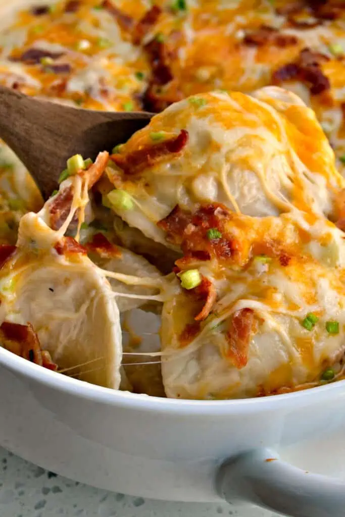 This family-friendly Cheesy Pierogi Casserole is layered with cheddar pierogies, creamy sauce, crisp bacon, scallions, mozzarella, and cheddar cheese.  This hearty casserole feeds six and takes less than fifteen minutes to get in the oven.