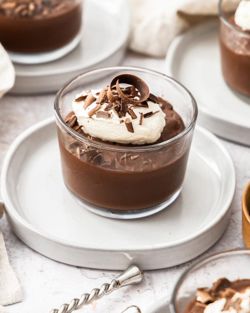 Four bowls of chocolate pudding with whipped cream and chocolate shavings.