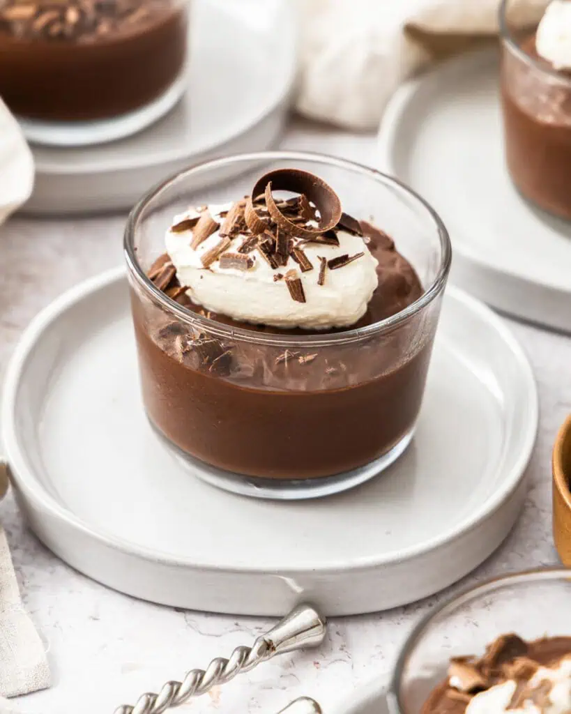 Four bowls of chocolate pudding with whipped cream and chocolate shavings. 