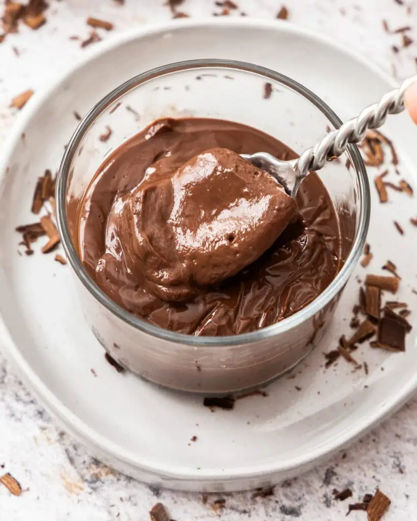 A spoon full of chocolate pudding in a single serving bowl. 