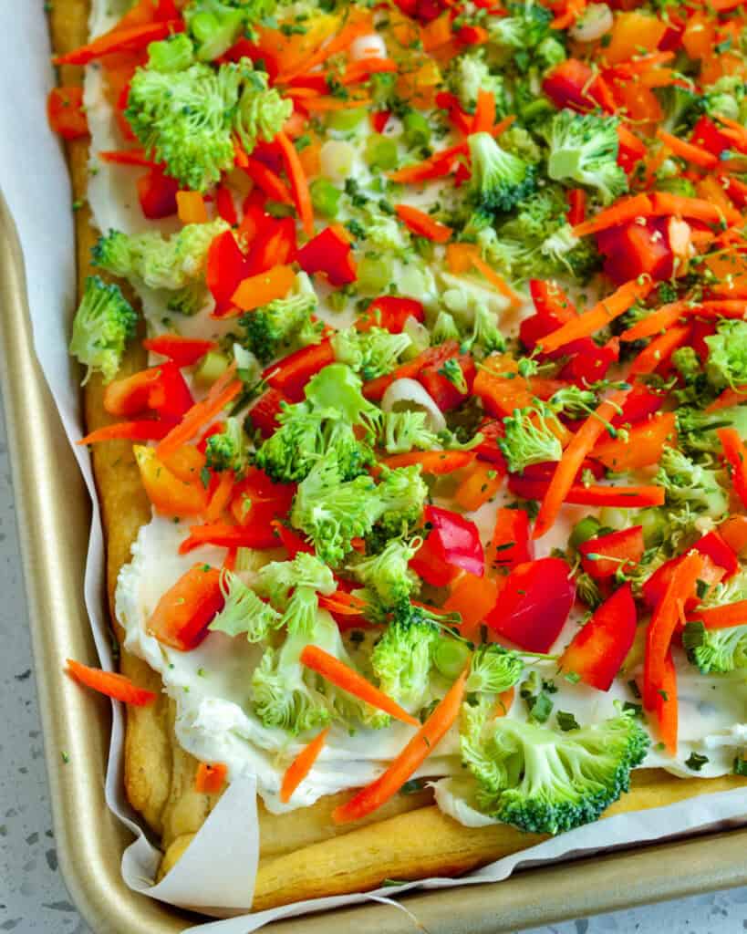 Cold Veggie Pizza Recipe with ranch cream cheese on a bakin sheet covered with parchment paper.