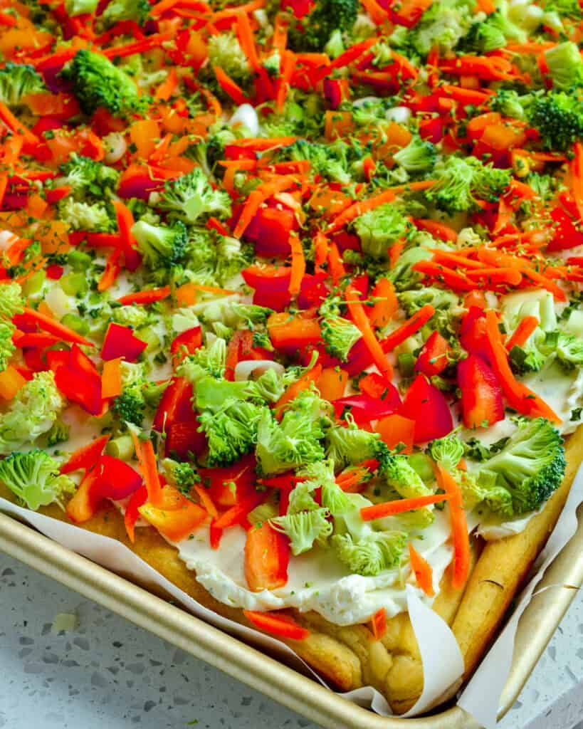 Cold vegetable cresent roll pizza on a parchment paper covered baking sheet.