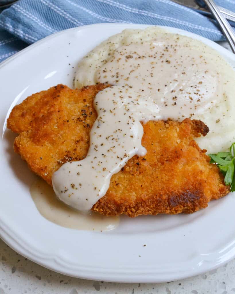 A breaded fried chicken breast and mashed potatoes smothered with rich country white gravy. 