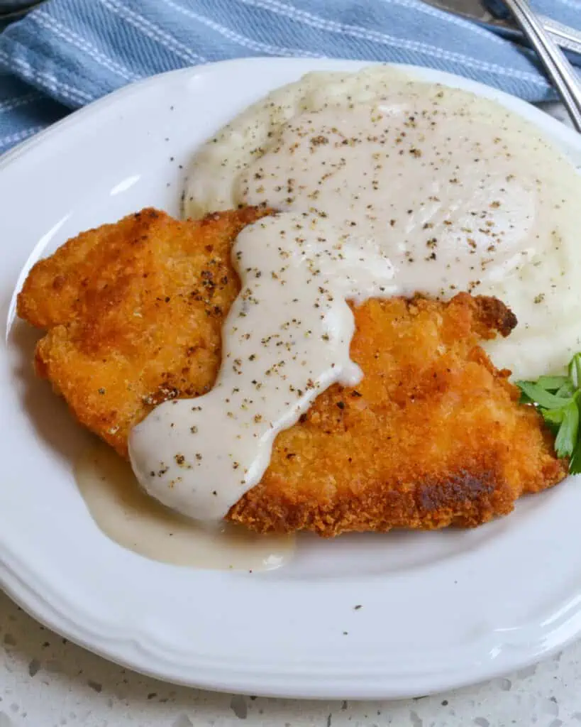 A breaded fried chicken breast and mashed potatoes smothered with rich country white gravy.