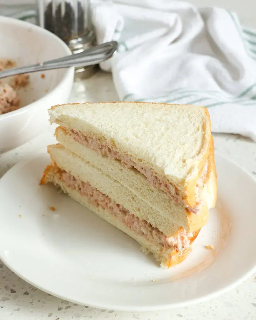 Deviled ham salad on white bread on a single serving plate with a bowl of deviled ham salad in the background. 